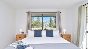 A bedroom with a large bed, two bedside tables, a window with curtains, and a view of trees. - Relaxing Rural Getaway – Near Kaiapoi Lakes, Room to Roam (Kaiapoi)