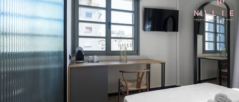 A hotel room with a bed, a desk with a chair, a TV mounted on the wall, and a window with a view of buildings.