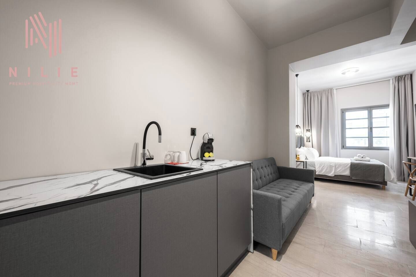 A modern kitchen with a built-in sink and a grey sofa in the living area.