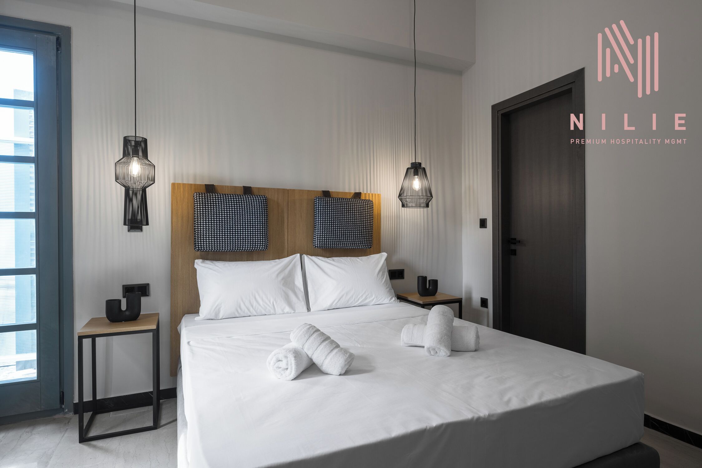 Camera d'albergo moderna con un grande letto, due comodini, una testiera in legno e due lampade a sospensione.