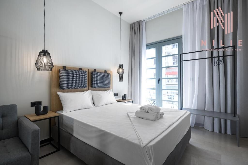 Ein modernes Hotelzimmer mit einem großen Bett, zwei Nachttischen, einem Sessel und einem Fenster mit Vorhängen.