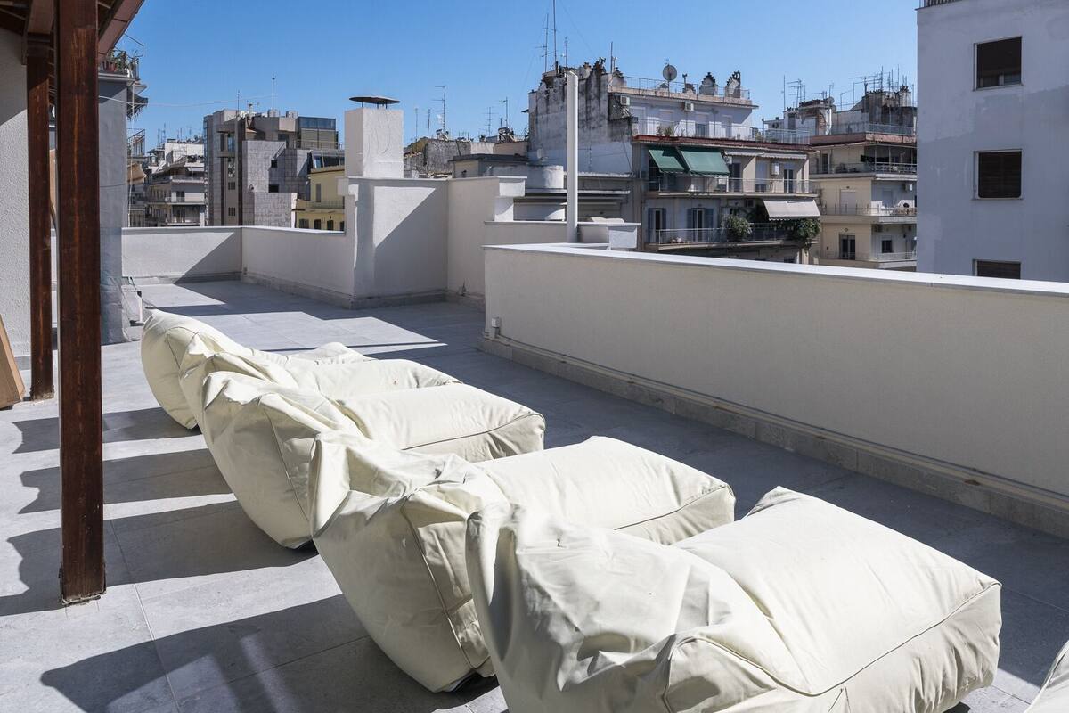 Terraza en la azotea con sillones reclinables cubiertos, una pérgola y vistas de edificios circundantes.