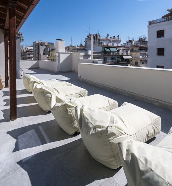 Terraza en la azotea con sillones reclinables cubiertos, una pérgola y vistas de edificios circundantes.
