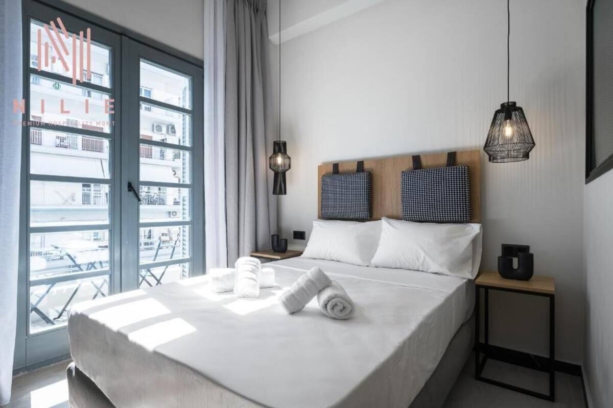 Habitación de hotel con una cama grande, dos almohadas, una mesita de noche, una lámpara y vistas al balcón exterior.