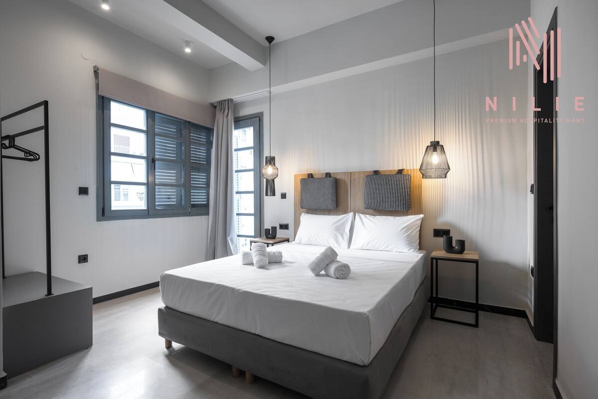 Una habitación de hotel moderna con una cama grande, mesitas de noche, un armario y vistas a la ciudad por la ventana.