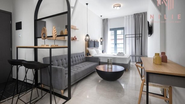 A modern hotel room with a sofa, a dining table, and a small kitchen area.