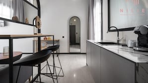 A modern kitchen with a central island, bar stools, a large window with a view, and a mirror reflecting the room.