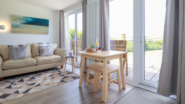 Una sala moderna con un sofá, una mesa de centro y una mesa de comedor. Hay un cuadro en la pared y vistas del exterior a través de amplias ventanas.