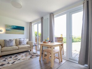 Un salon moderne avec un canapé, une table basse et une table à manger. Un tableau orne le mur et de grandes fenêtres offrent une vue sur l’extérieur.