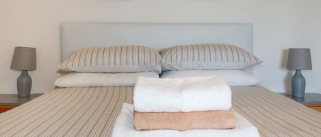 Un letto rifatto con cuscini a righe, una pila di asciugamani piegati e due quadri appesi al muro.