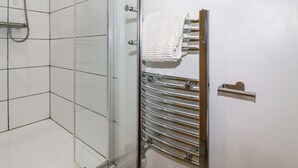 Un baño con cabina de ducha de vidrio, un perchero cromado con una toalla blanca y pared de azulejos blancos.