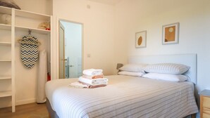 Una cama bien hecha con toallas dobladas, un armario blanco y una puerta que da a un baño.
