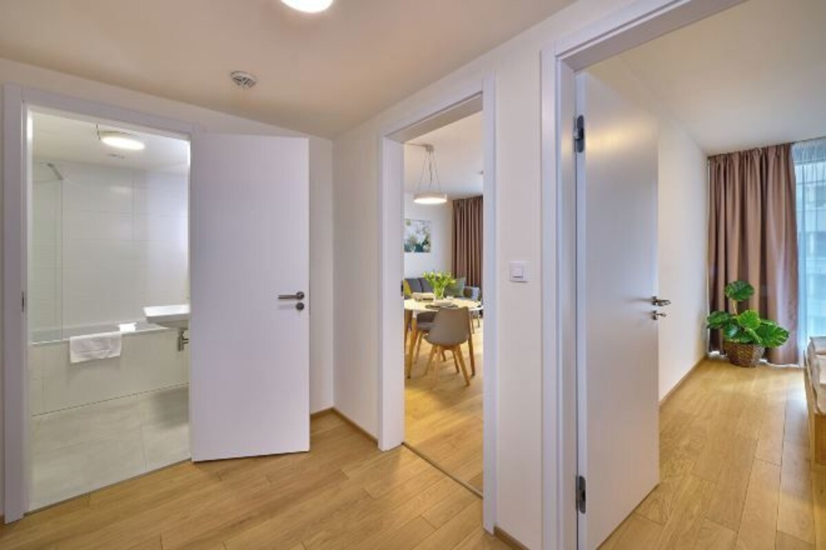 A hotel room with a wooden floor, a bathroom with a shower, and a dining area visible through an open door.