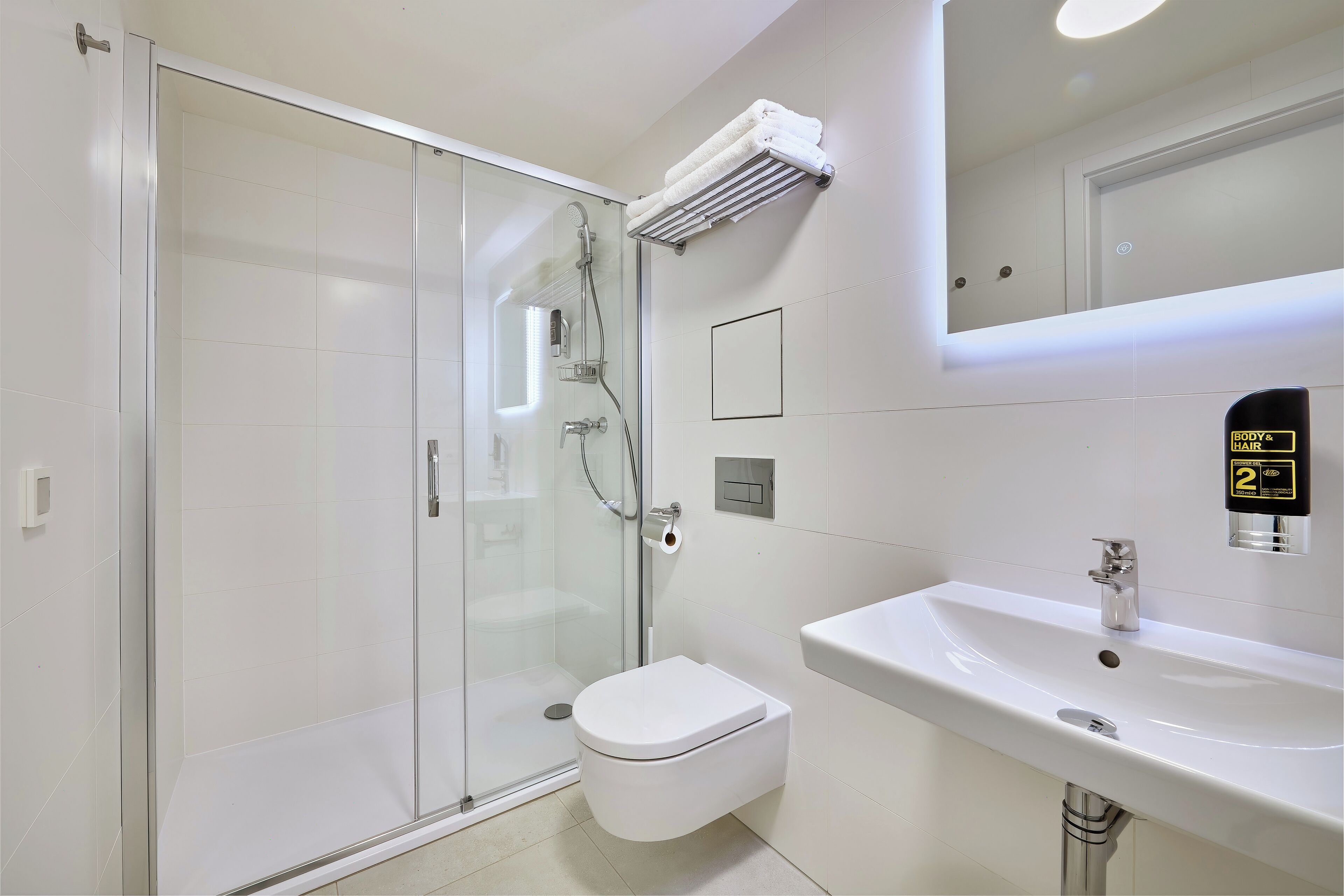 Un baño moderno con cabina de ducha de vidrio, inodoro blanco y lavamanos con espejo.