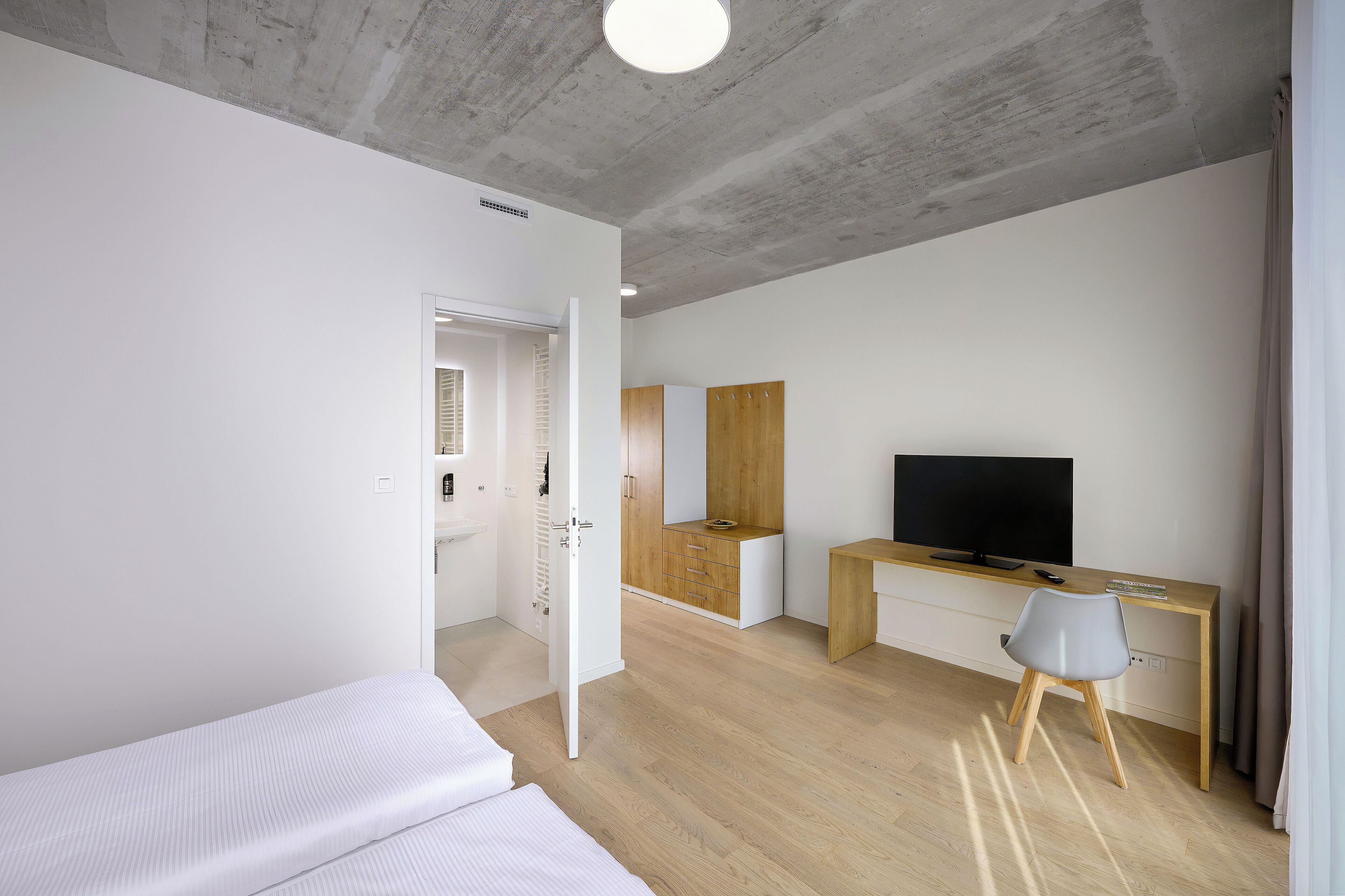 Ein modernes Schlafzimmer mit Bett, Schreibtisch, Stuhl, Fernseher und Kleiderschrank.