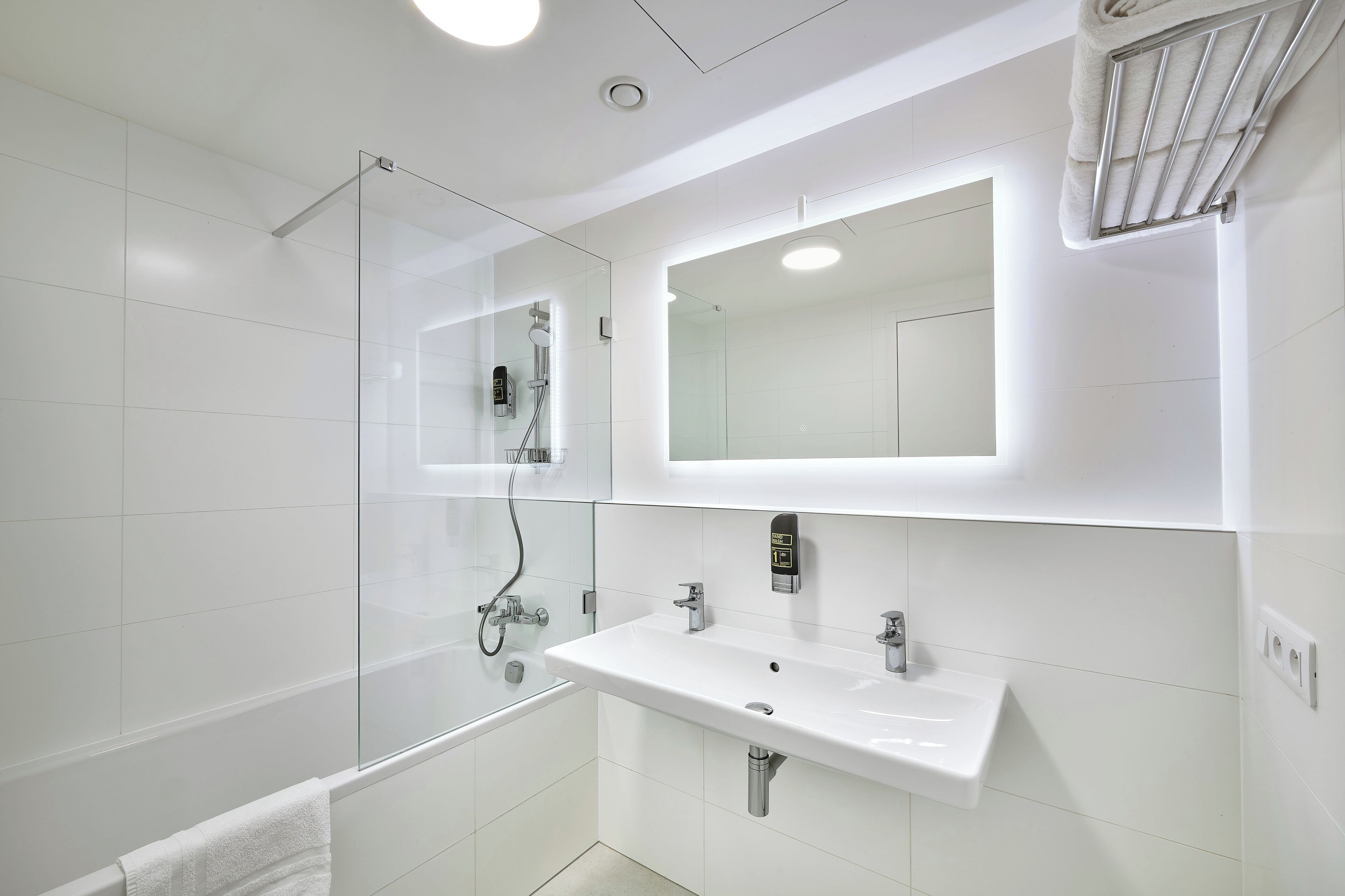 Un baño moderno con cabina de ducha de vidrio, un lavamanos blanco y un espejo sobre él.
