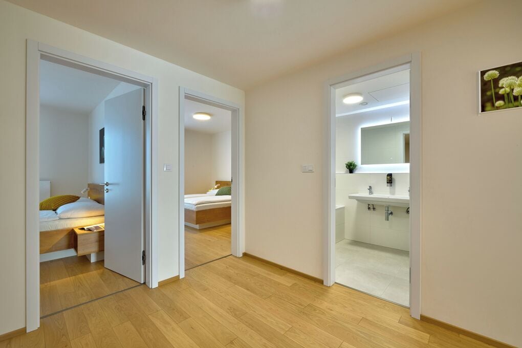 Une chambre d’hôtel moderne avec un plancher en bois, un lit doté d’une table de chevet, une table de nuit et une salle de bain avec un lavabo et un miroir.