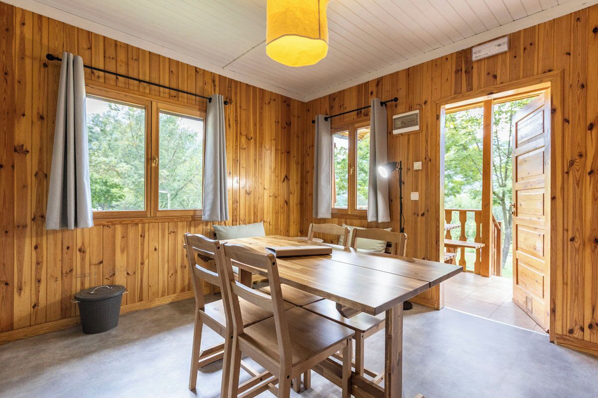 A wooden cabin with a dining table and chairs, large windows, and a view of the outdoors.