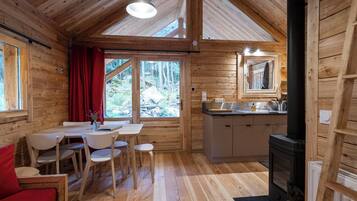 A wooden cabin interior with a dining area, kitchen, and a fireplace.