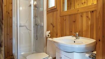 Ein Badezimmer mit Holzwänden, einer Glasdusche, einer weißen Toilette und einem Waschbecken mit Spiegel darüber.