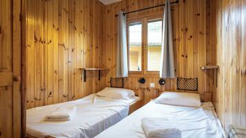 Habitació d'una cabana de fusta amb dos llits, una finestra amb cortines i una petita estant.
