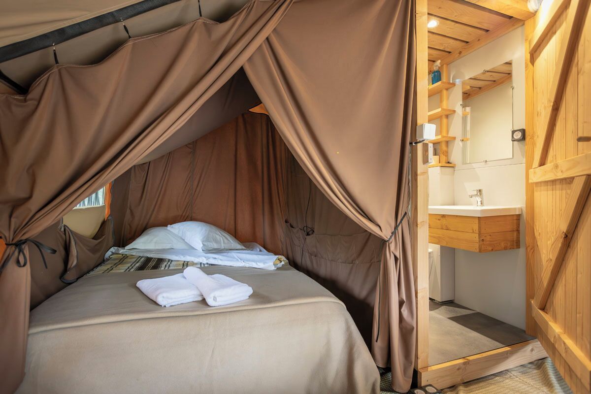 A tent-style bedroom with a bed, towels, and a wooden interior.