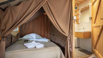 A tent-style bedroom with a bed, towels, and a wooden interior.