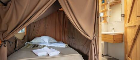 A tent-style bedroom with a bed, towels, and a wooden interior.