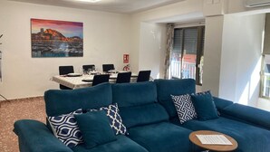 A living room with a blue sofa, a dining table with chairs, a painting on the wall, and an air conditioning unit. - Family Apartment near ADDA | Breakfast Included | Sleeps 7 (Alicante (Alacant))