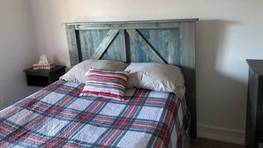 A bed with a plaid bedspread and two pillows, a wooden headboard, a bedside table with a tissue box, and a nightstand.
