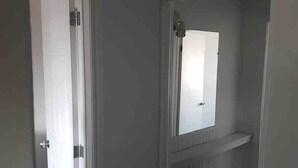 A narrow hallway with a white door on the left, a small mirror on the right, and a radiator below.
