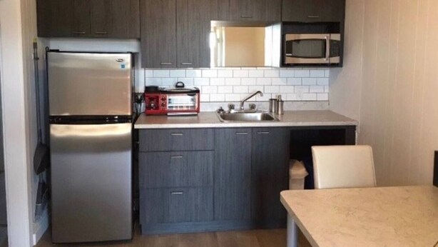 A compact kitchen with dark cabinets, a stainless steel refrigerator, a microwave, and a small countertop with a sink.