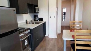 Una cocina compacta equipada con refrigerador, estufa, microondas y un pequeño comedor con mesa y sillas.
