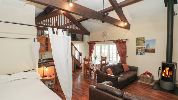 A cozy living room with a fireplace, a dining area, and a staircase leading to an upper level. - Oakenbank Barn (Macclesfield)