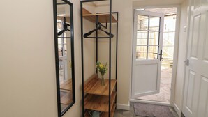 A hallway with a wooden shelf unit, a mirror, and a door leading outside. - Oakenbank Barn (Macclesfield)
