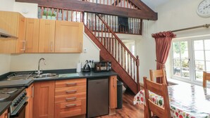 A kitchen with wooden cabinets, a dishwasher, a stove, and a dining area with a table and chairs. - Oakenbank Barn (Macclesfield)