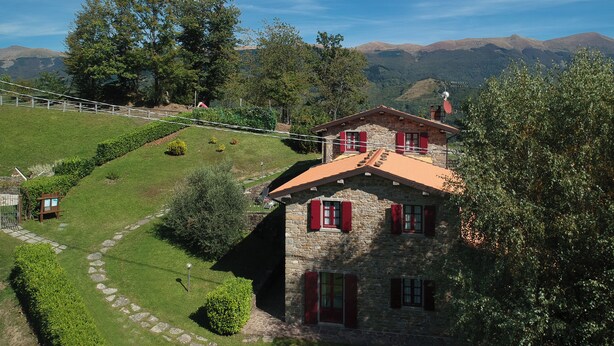 A stone house with red shutters, surrounded by a well-maintained garden and a scenic mountain backdrop. - La Vecchia Fornace La Piastra Apartments (Abetone Cutigliano)