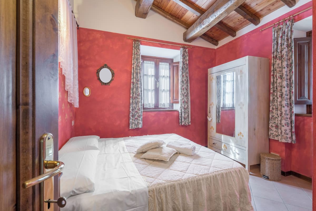 A bedroom with a bed, a wardrobe, a mirror, and a window with curtains.