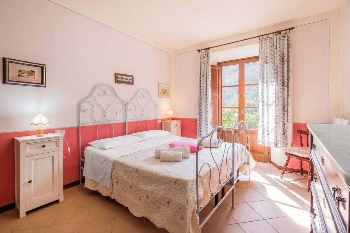 A bedroom with a bed, bedside table, lamp, and a window with curtains.