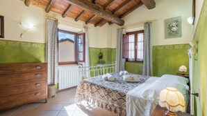 A bedroom with a wooden ceiling, a bed with a patterned bedspread, a nightstand with a lamp, and a dresser. - La Vecchia Fornace La Piastra Apartments (Abetone Cutigliano)