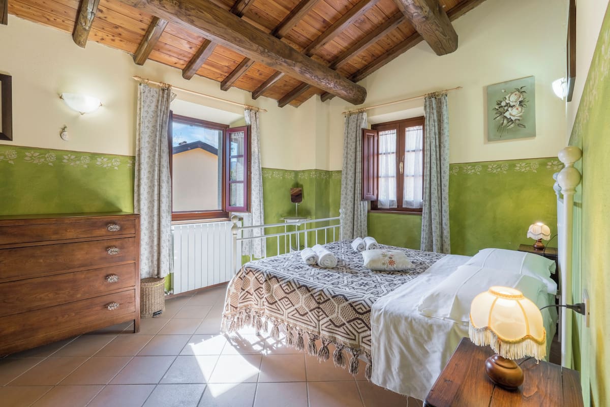 A bedroom with a wooden ceiling, a bed with a patterned bedspread, a nightstand with a lamp, and a dresser.