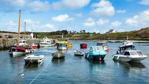 A harbor with various boats docked, a lighthouse, and a white house on a hill. - 5 Sea View Street (Cemaes Bay)