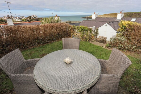 A round wicker table with four chairs in a garden with a view of the sea and houses.