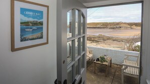 A room with a large window overlooking a beach, a framed picture on the wall, and a small table with chairs outside. - 5 Sea View Street (Cemaes Bay)