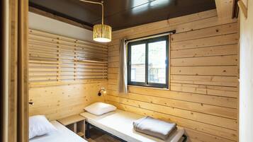Una habitación de cabaña de madera con cama, un banco, una ventana y una lámpara colgante.