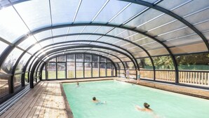 Une piscine couverte dotée d’une terrasse en bois et de panneaux de verre.