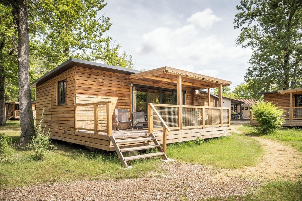 Una cabaña de madera con terraza, porche cubierto y un pequeño espacio para sentarse al aire libre.