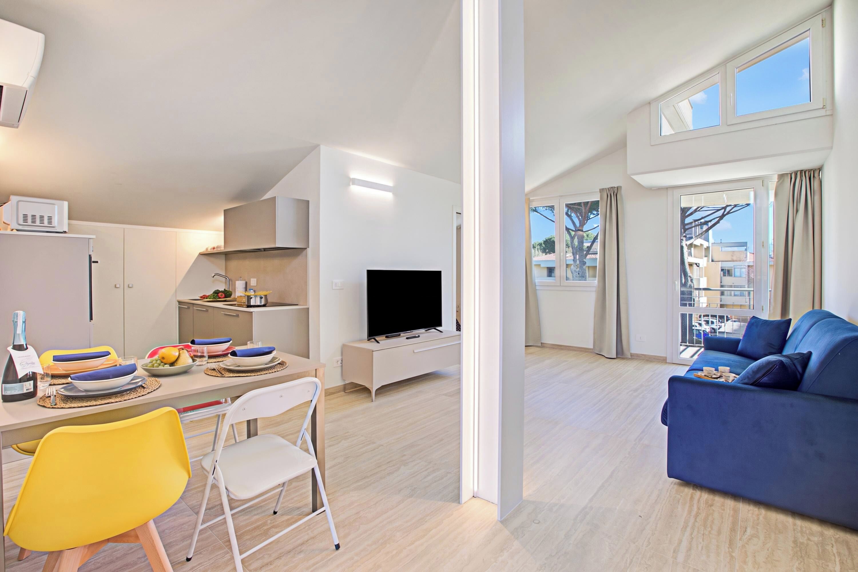 A modern living room with a flat-screen TV, a sofa, and a dining area with a table set for two.