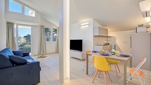 Un appartement moderne comprenant un salon, un coin repas et une cuisine. Il est équipé d’un canapé, d’une table à manger, de chaises, d’un téléviseur et d’un réfrigérateur.