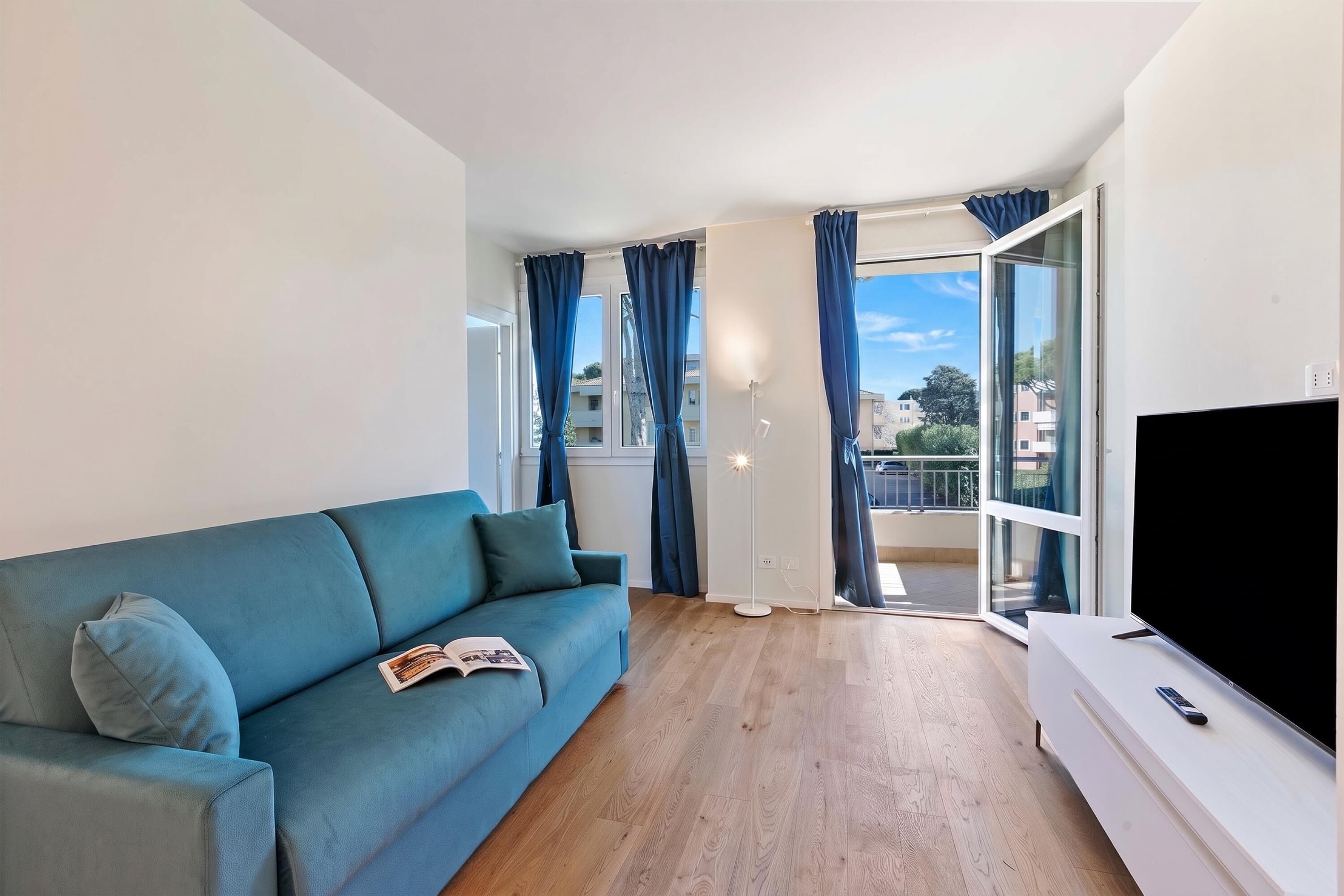 A living room with a sofa, a flat-screen TV, and a balcony with curtains.